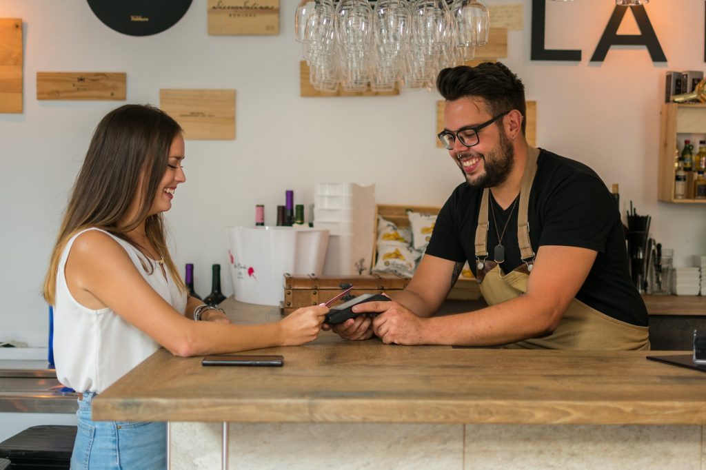 A young woman pays with credit card in a pub. The waiter holds a credit card terminal