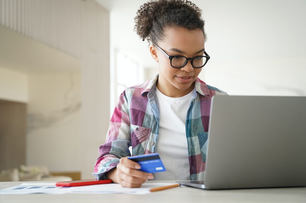 African american young girl holding credit card makes payment uses online banking services on laptop