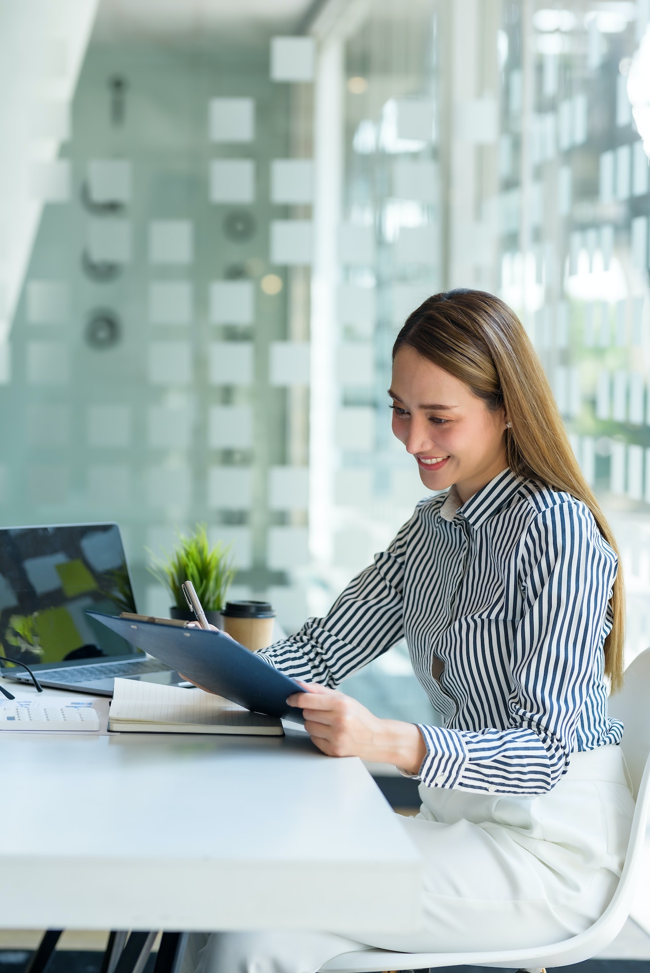 Beautiful Asian businesswoman using her laptop enjoys working, taking notes, reviewing assignment