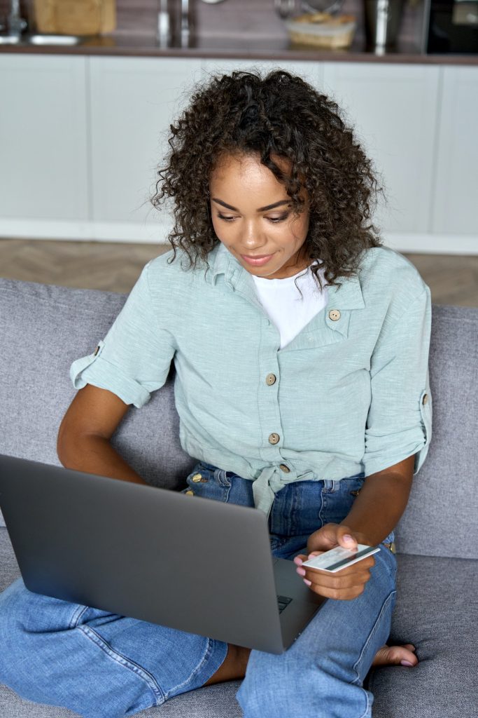 Young adult African american girl sitting indoors doing mobile payment online.